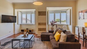 A living room with a sofa, a coffee table, a TV, and a window with a view. - Spacious Mordern Apt in Graça’s Historic Quarter (Lisbon)