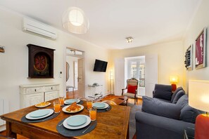 Ein Essbereich mit einem Holztisch, gedeckt für das Frühstück, einer Couch und einem Fernseher an der Wand.