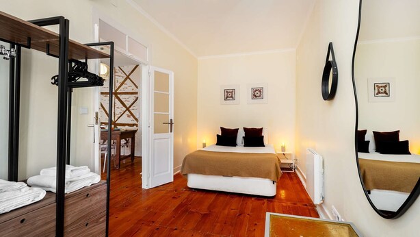 Een hotelkamer met een houten vloer, een bed met donkere beddengoed, een grote spiegel en een deur naar een badkamer.