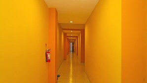 A long, narrow hallway with yellow walls and a tiled floor, leading to a door at the end.