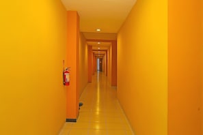 A long, narrow hallway with yellow walls and a tiled floor, leading to a door at the end.