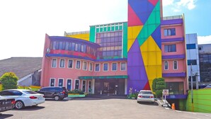 A multi-story hotel with a colorful facade, a prominent vertical sign, and a parking area with several cars. - Stylish DBL Suite Escape W/ Free WiFi and Parking (Jakarta)