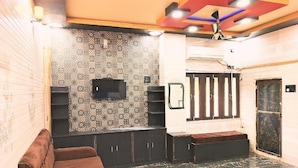 A room with a patterned wall, a flat-screen TV, a brown sofa, and a patterned rug. - Atharv Paying Guest House (Varanasi)