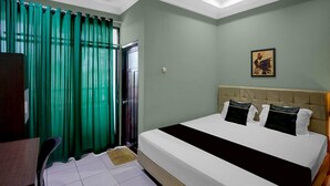 A hotel room with a bed, a desk, a chair, a window with curtains, and a wall-mounted picture.