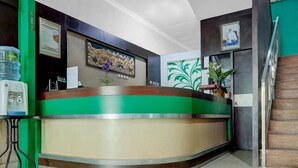 A reception desk with a green and beige color scheme, a framed picture on the wall, a water dispenser, and a staircase to the right.