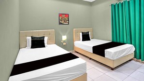 Dos camas con cabeceros, una lámpara de pared, un cuadro y cortinas verdes.