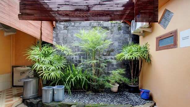 Une cour intérieure agrémentée de plantes en pot, un mur de pierre et une plaque indiquant le numéro d’une pièce.