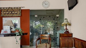 A hotel reception area with a desk, a chair, a sofa, a clock, and a decorative curtain.