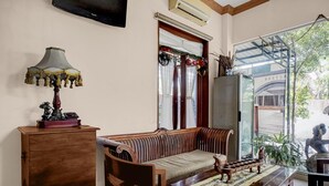 A traditional wooden sofa, a wooden cabinet, a table with a patterned tablecloth, and a window with curtains.