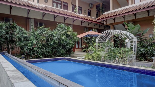 A swimming pool with a tiled border, surrounded by lush greenery and a white decorative structure.