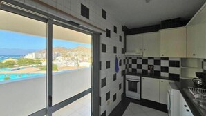Una cocina con vistas a una piscina y edificios, armarios blancos y salpicadero de azulejos.
