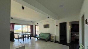 Una habitación amplia con un sofá verde, una mesa de comedor con sillas y vistas a través de ventanas grandes.