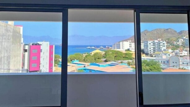 Vista desde una ventana con cielo despejado, edificios y montañas a lo lejos.