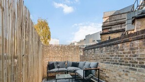 A patio with a sofa, table, and a bamboo fence. - Modern Fulham 1-bedroom Apartment (London)