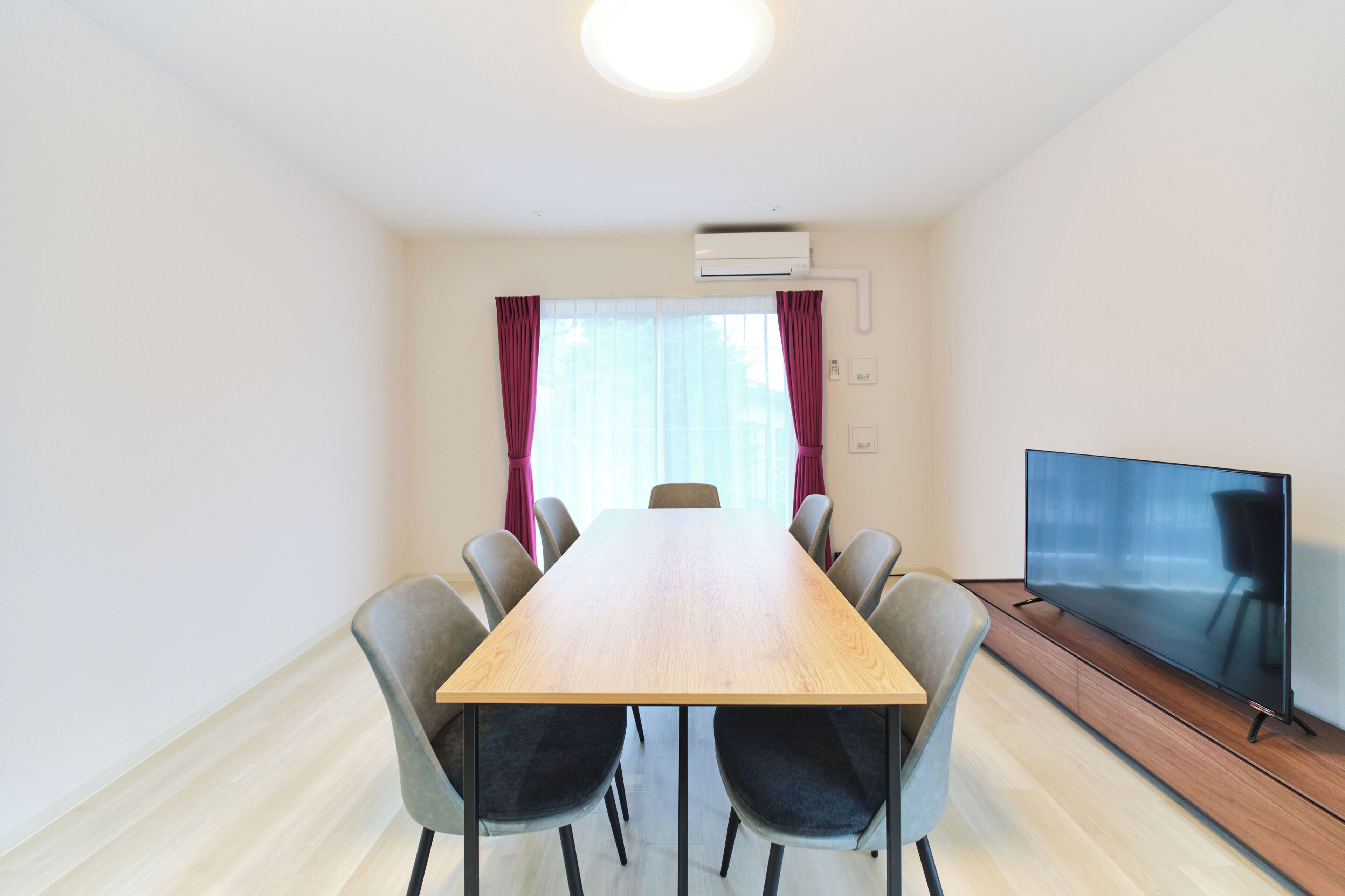 Un salón de conferencias con una mesa de madera, seis sillas, un televisor de pantalla plana y un equipo de aire acondicionado.
