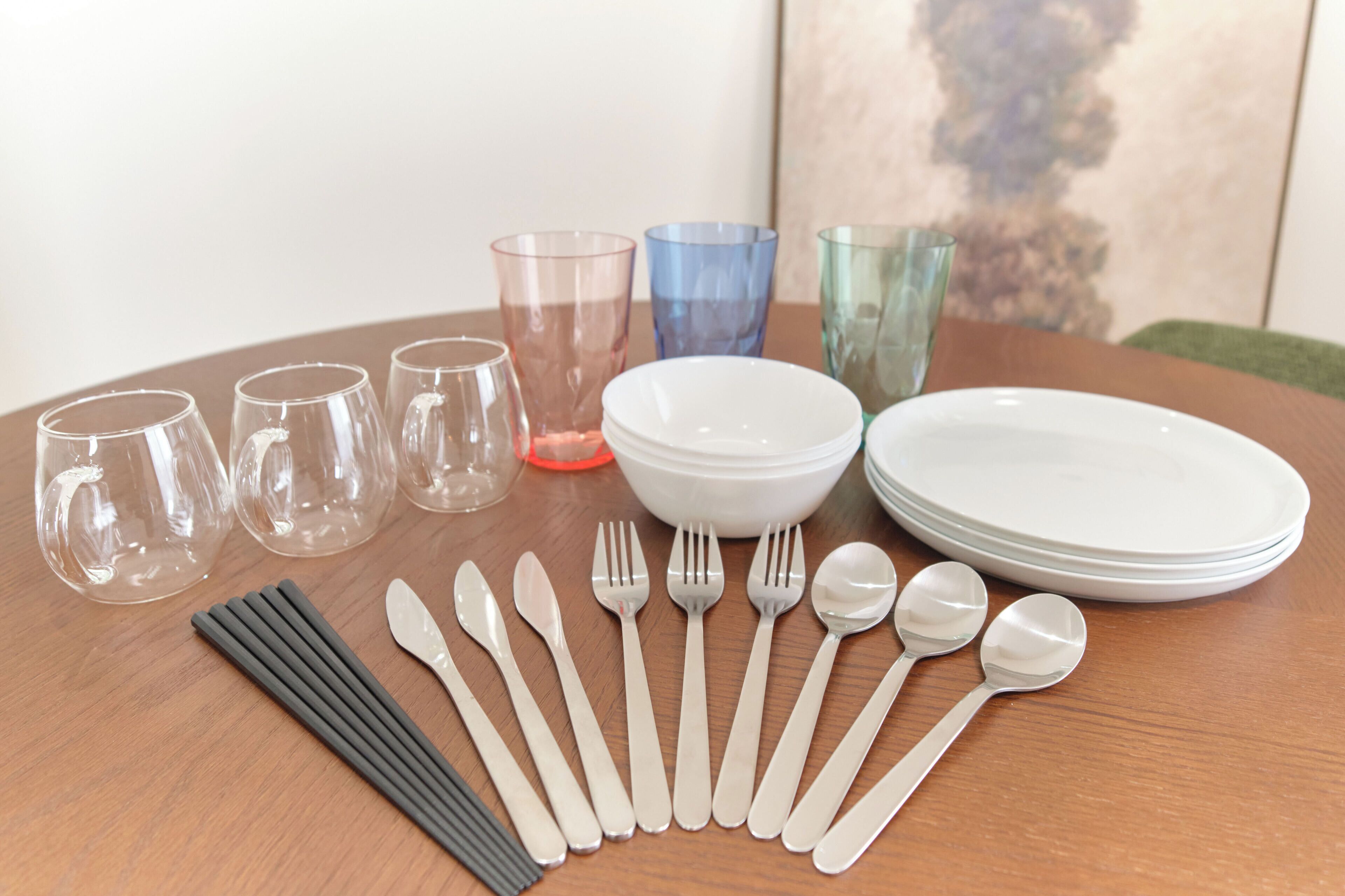 Una mesa de comedor con vasos transparentes, platos, cubiertos y un tazón.