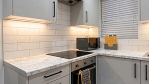 A kitchen with white cabinets, a microwave, a stove, and a window with blinds. - Newly refurbished London base with Jubilee line on your doorstep (Greater London)