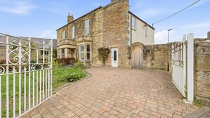 A stone building with a paved driveway and a white metal gate.
