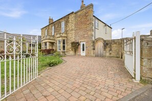 A stone building with a paved driveway and a white metal gate.