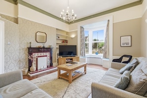 A living room with a fireplace, television, sofa, and a large window with curtains.