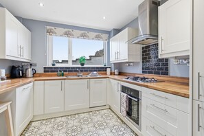 A modern kitchen with white cabinets, a wooden countertop, a gas stove, and a window with a view. - Idlewyld - North East Escapes (Amble)