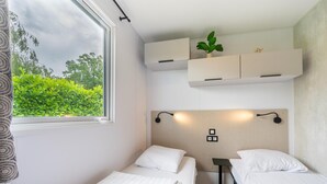 A bedroom with two beds, a window with a view of greenery, built-in cabinets, and a wall-mounted light fixture.
