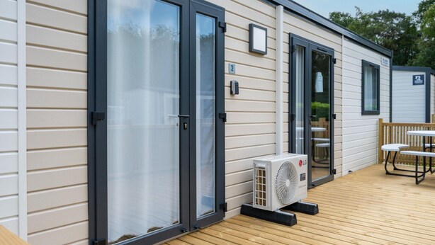A mobile home with a sliding glass door, a patio with a table and chairs, and an air conditioning unit.