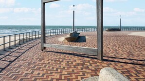 A paved promenade with a metal railing, a stone bench, and a wooden frame structure.