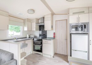 A compact kitchen with a built-in oven, a microwave, and a refrigerator. - Gold 3 Bedroom Caravan, Sleeps 8. With decking (Clacton-on-Sea)