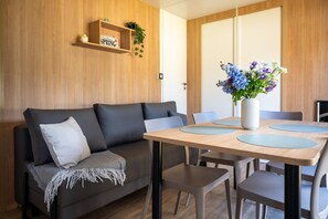 A modern living room with a sofa, a dining table with chairs, and a wall-mounted shelf with a sign.