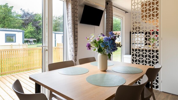 A dining area with a table, chairs, a vase of flowers, and a TV mounted on the wall.