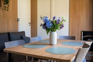 Un comedor con una mesa de madera, individuales azules y un jarrón blanco con flores.