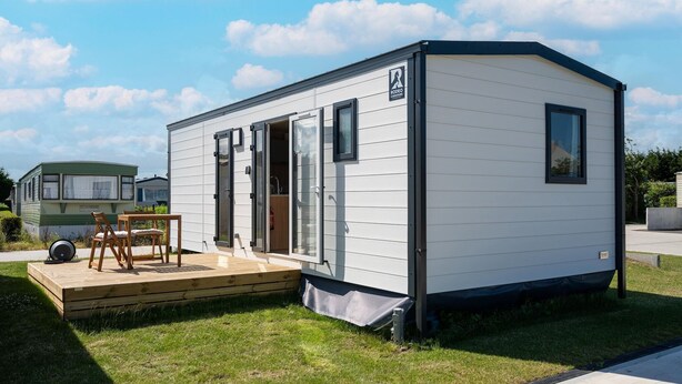 A mobile home with a deck, a table, and chairs.
