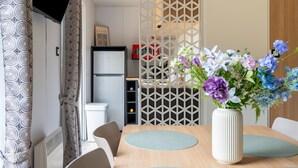 A dining area with a table, chairs, a vase with flowers, a refrigerator, and a patterned curtain.
