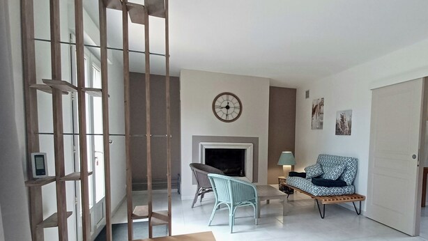 A living room with a fireplace, a clock on the wall, and a door leading to another room. - Gîte in the heart of nature, peace and quiet guaranteed, animals welcome. (Diges)