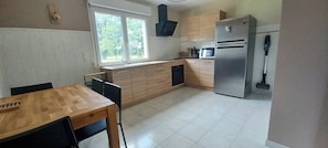Eine Küche mit Holztisch, Stühlen, einem Kühlschrank, einer Mikrowelle und einem Fenster mit Blick auf Bäume.