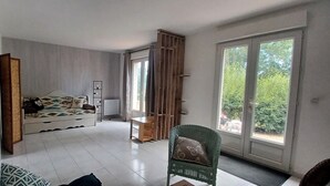 A room with a bed, a chair, a small table, and a sliding glass door leading to a balcony. - Gîte in the heart of nature, peace and quiet guaranteed, animals welcome. (Diges)