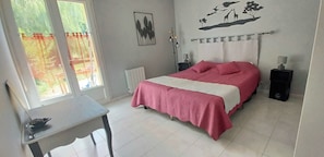 Ein Schlafzimmer mit Bett, Nachttischen, einem Heizkörper, einem Fenster mit Vorhängen und einer Wanddekoration.