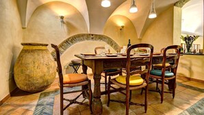 A dining area with a rustic wooden table, chairs with cushioned seats, a large vase, and a stone archway. - Guest house Cà du Sciu Megu (Civezza)