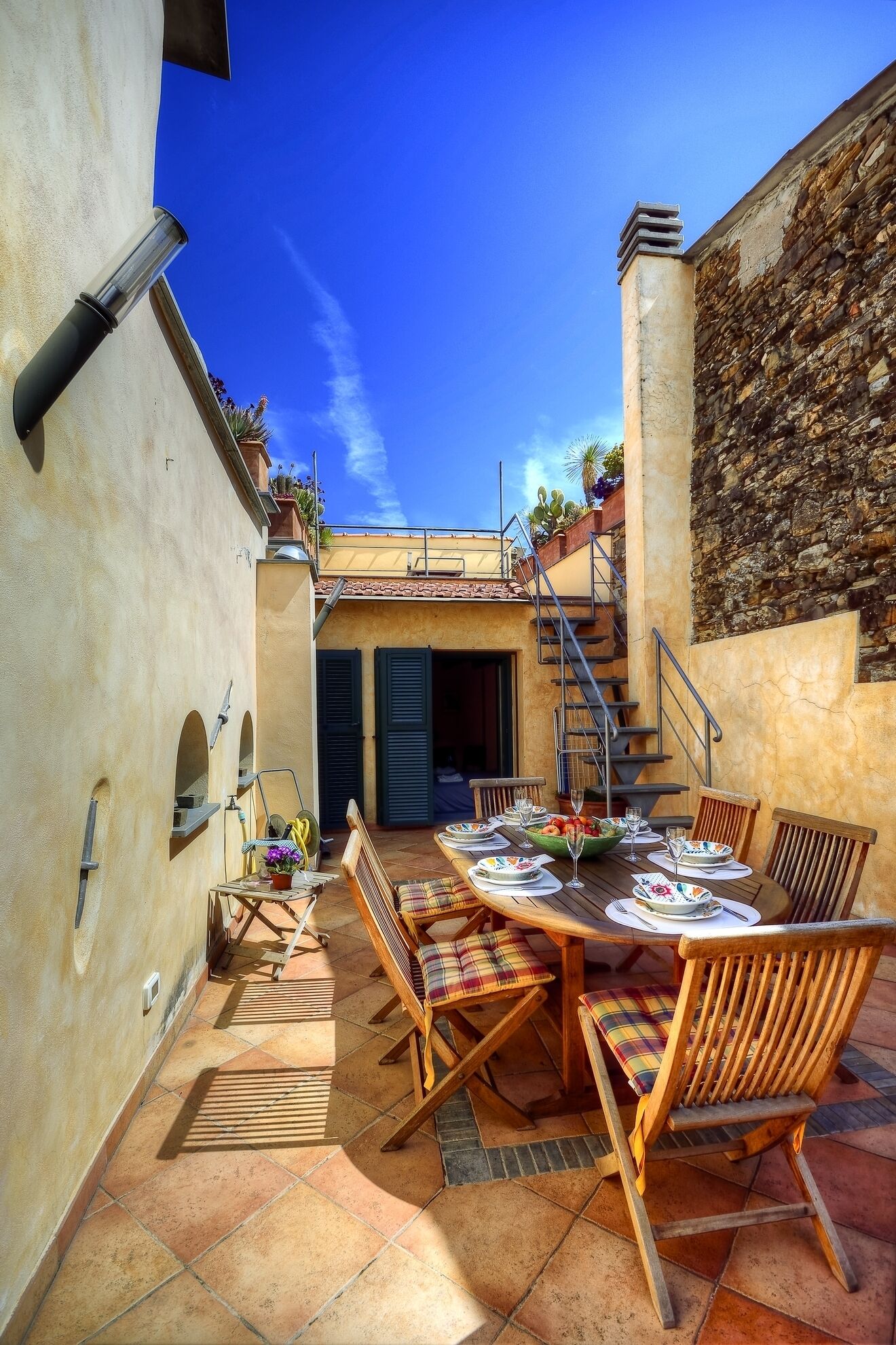 An outdoor patio with a round table set for dining, surrounded by wooden chairs.