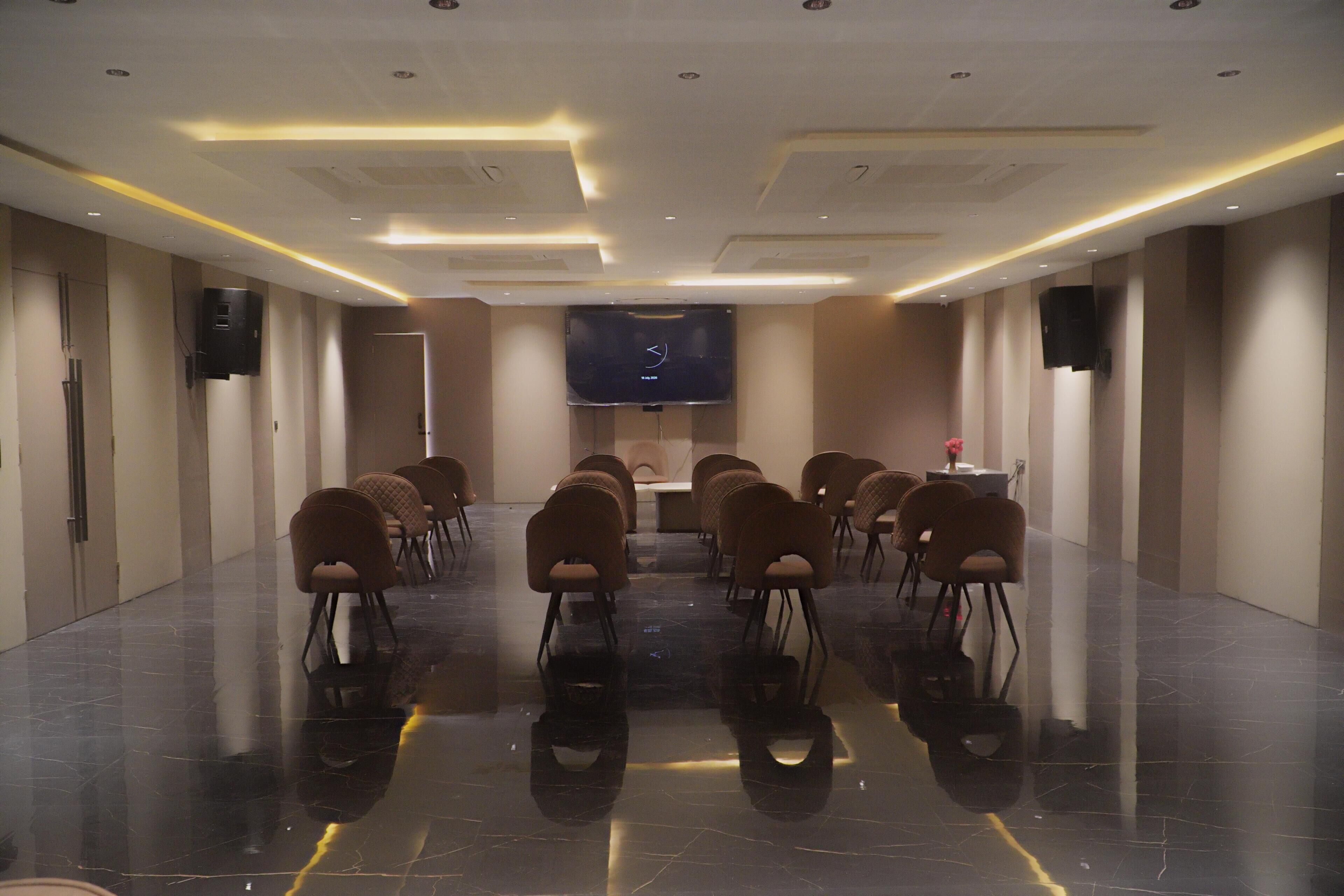 A conference room with a large flat-screen TV at the front, arranged seating, and a polished floor.