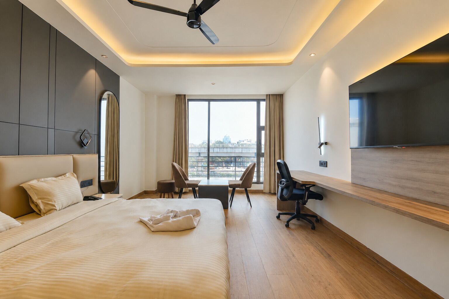 A modern hotel room with a large bed, a desk, a chair, a flat-screen TV, and a ceiling fan.