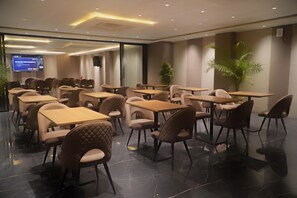 A conference room with tables and chairs, a television screen, and a plant. - Melange Hotel - Golf course road (Gurugram)