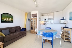 Ein kompakter Wohnbereich mit einer Couch, einem Esstisch, Stühlen, einer Küchenzeile und einem Schrank.