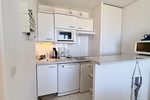 Eine kompakte Küche mit weißen Schränken, einer eingebauten Mikrowelle, einer Kaffeemaschine und einem Geschirrspüler.
