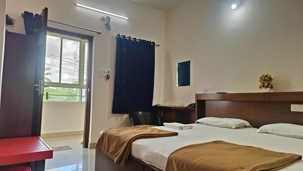 A hotel room with a bed, bedside table, and a window with curtains. - Binayak Palace OD (Kendrapara)