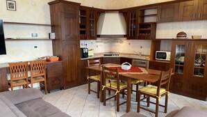 A compact kitchen with wooden cabinets, a dining table, and a sofa. - Apartment Ramina (San Giuseppe - Comacchio)