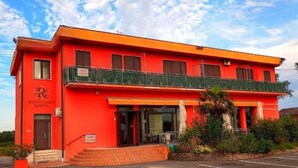 A red building with a balcony, a sign reading 'Affitta Camere Ramina,' and a parking lot. - Apartment Ramina (San Giuseppe - Comacchio)