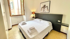 Ein Hotelzimmer mit einem Bett, einem Nachttisch, einer Lampe, einem gerahmten Bild und einem Fenster mit geöffneten Rollläden.