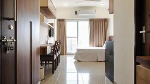 A hotel room with a bed, a desk, a chair, a TV, and a balcony with curtains.